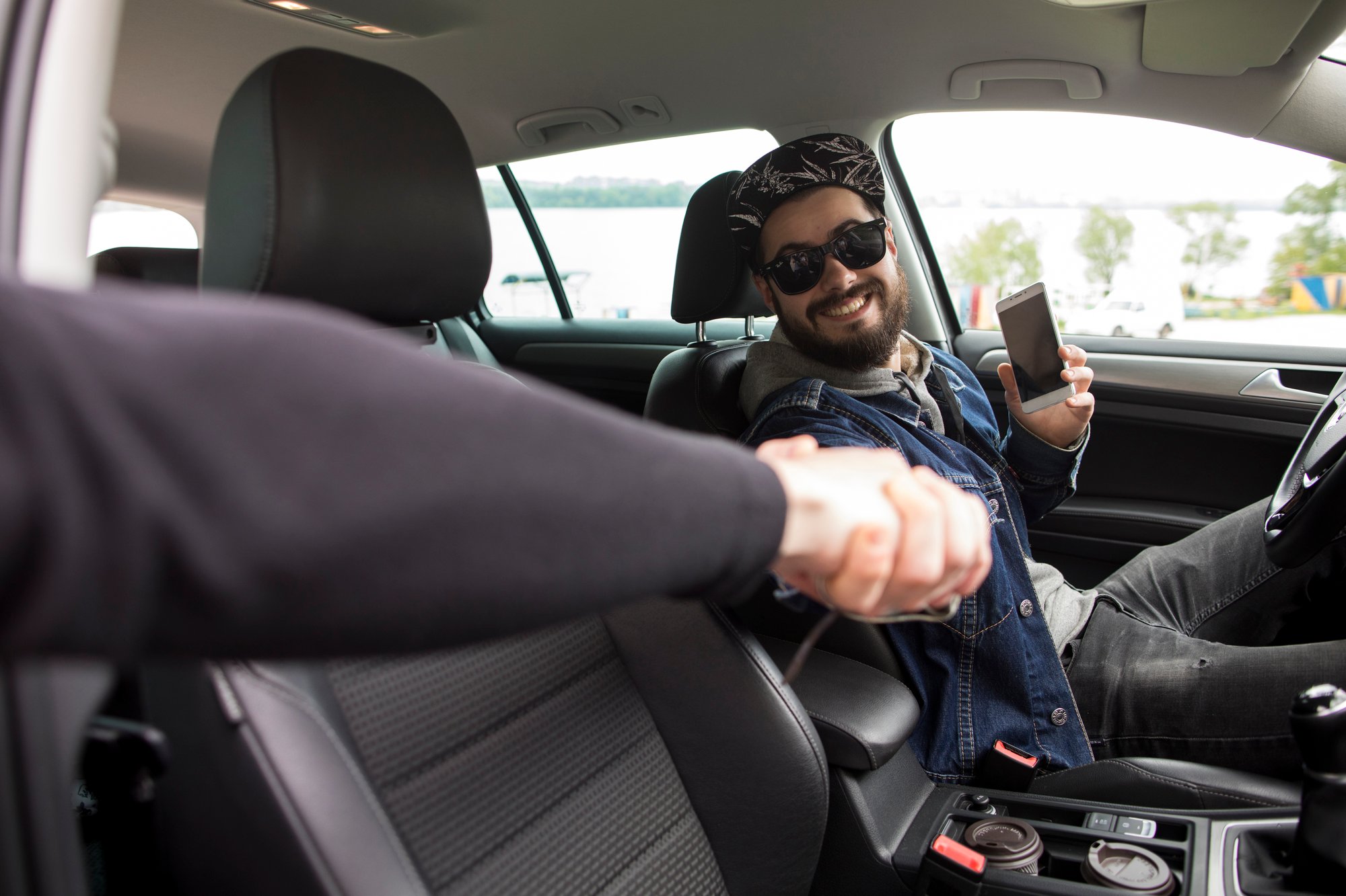 young-man-with-phone-greeting-friend-while-sitting-car